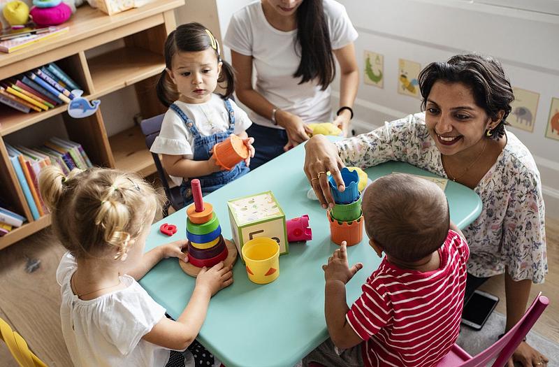 Early years practitioner sitting on floor and playing with three children around a small table